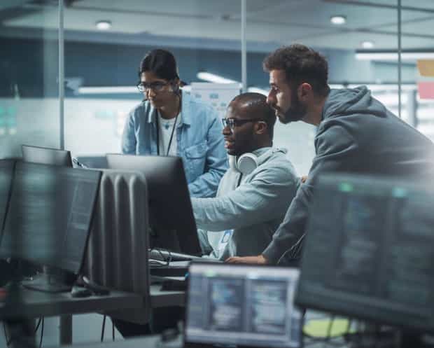 Three people collaborating in a modern office, illustrating software asset management through teamwork and IT monitoring.
