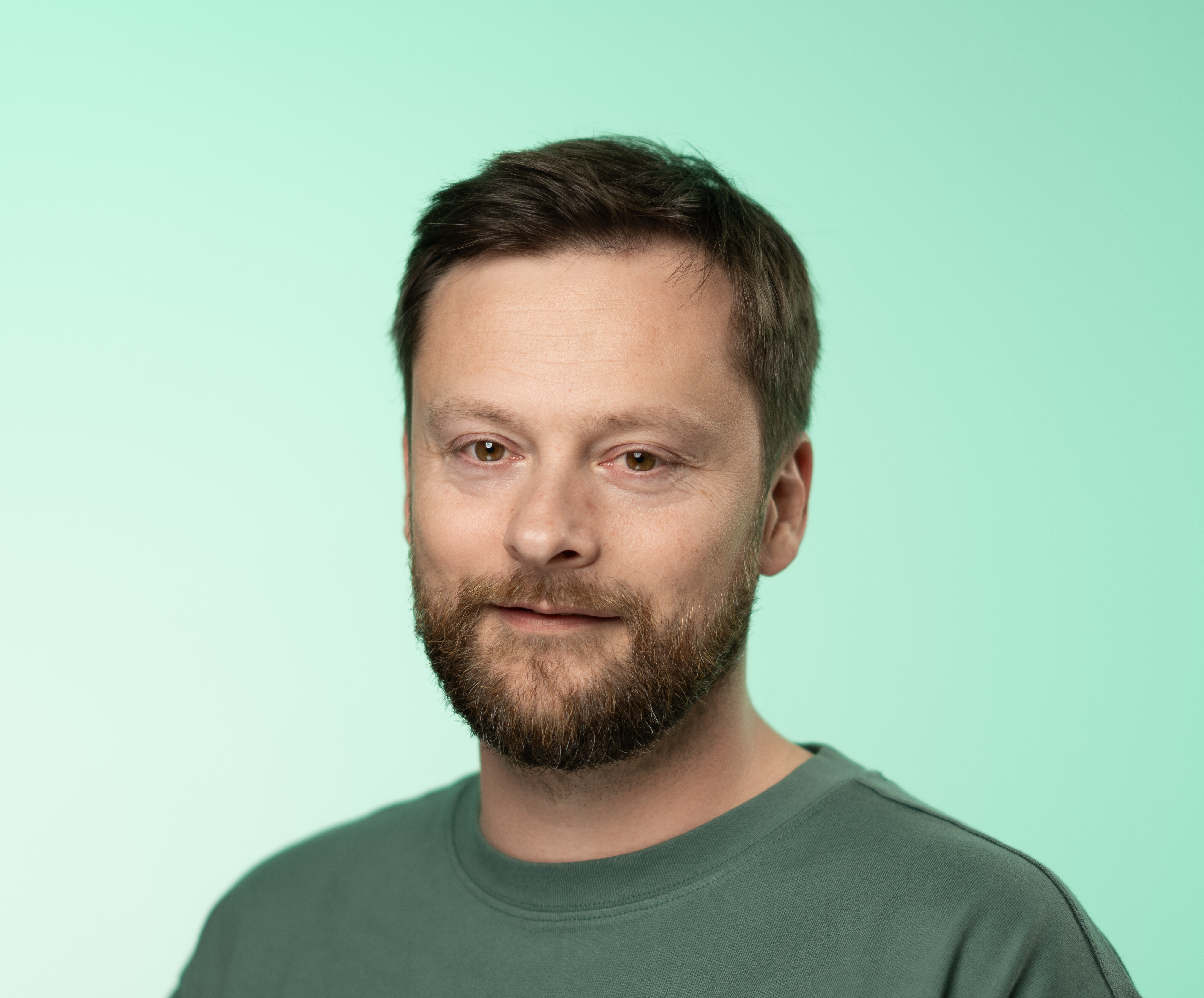 Portraitbild einer Person in einem grünen Oberteil vor einem hellgrünen Hintergrund.