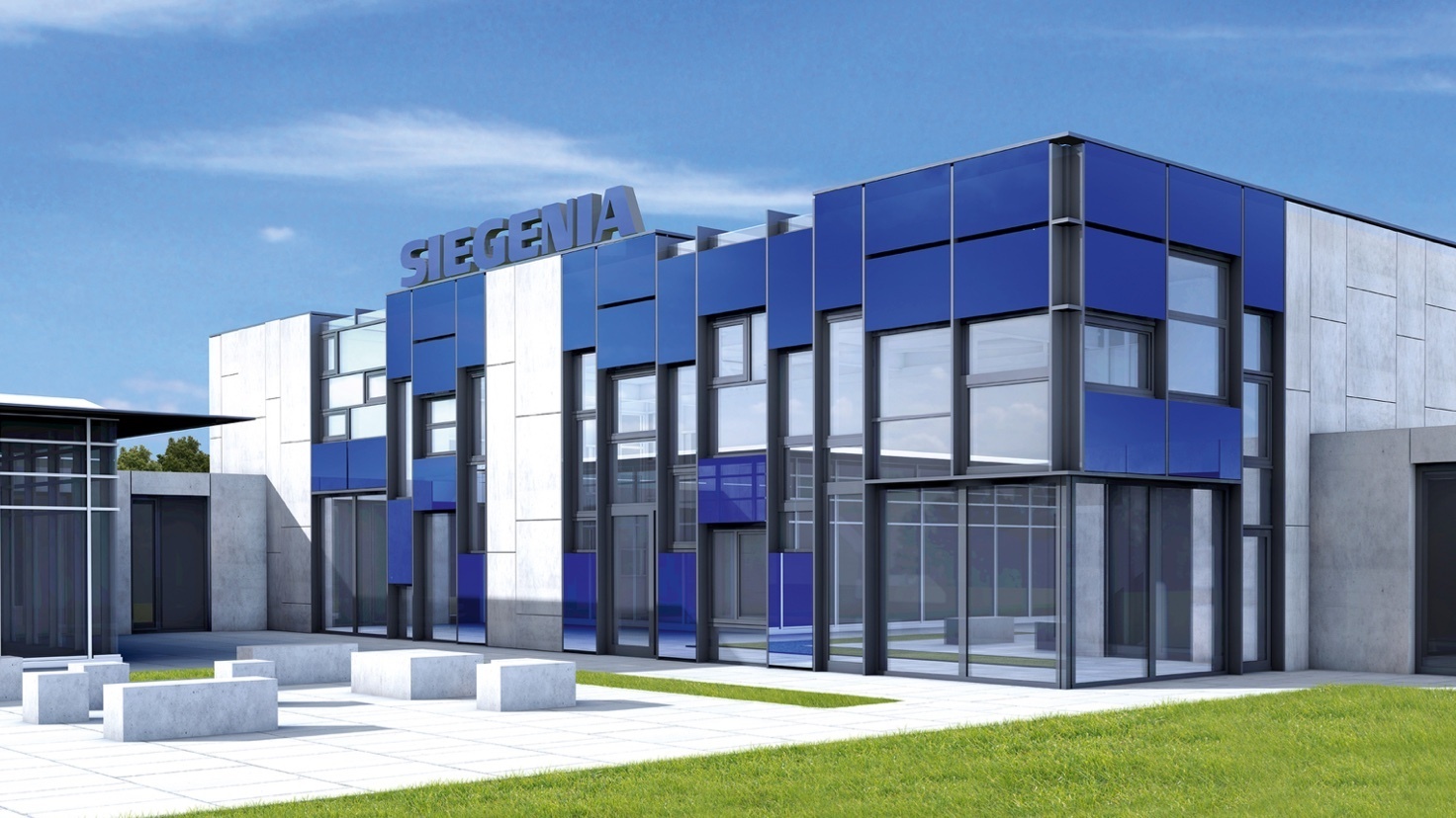 Exterior view of a modern industrial building with blue and white façades, large glass windows, and clean geometric lines. The building stands on a paved area with grass and concrete elements.
