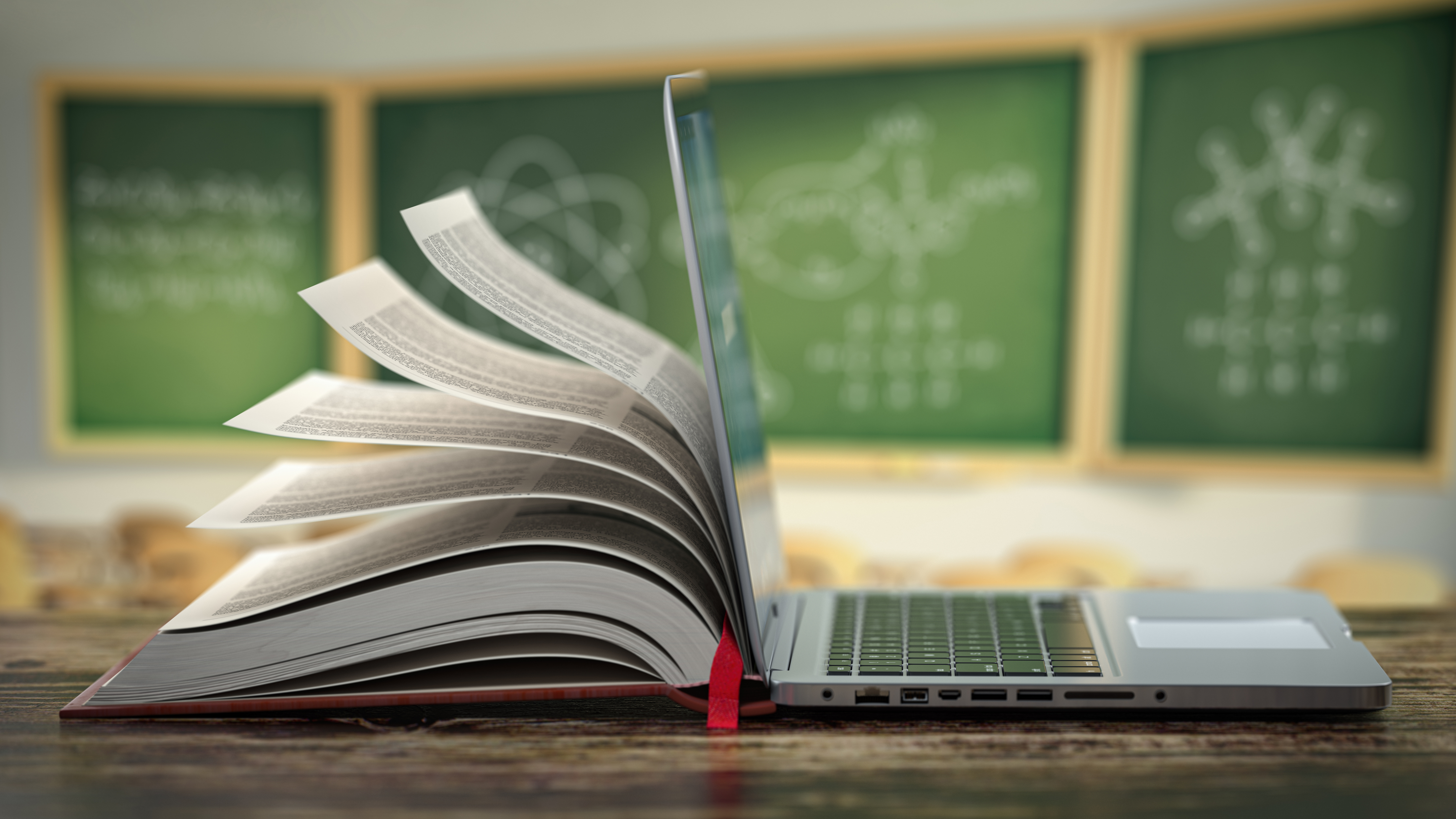 Offener Laptop und Bücherstapel in einem Klassenzimmer.