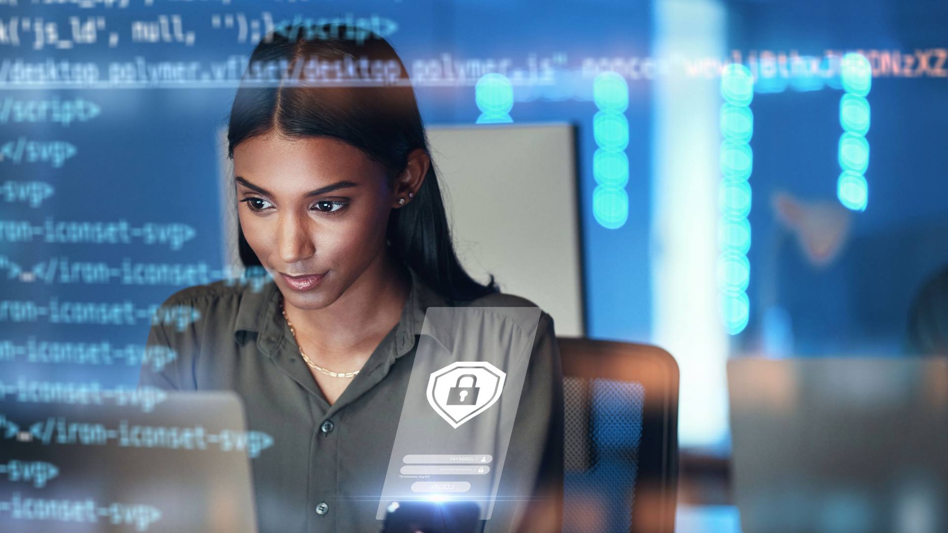 Una persona è seduta davanti a una postazione di lavoro con un computer; sull’immagine sono sovrapposti elementi di interfaccia relativi al codice e alla sicurezza. In primo piano è visibile l’icona di uno scudo con un lucchetto, mentre sullo sfondo compaiono codici digitali e display illuminati di blu.